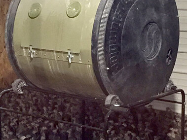 A composter located in brooder facility with birds surrounding the base of the unit.