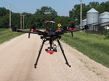 A drone taking off, flying low along a gravel road.